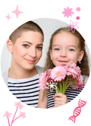 Una madre con cáncer de mama sonriendo junto a su pequeña hija, quien sostiene unas flores rosas